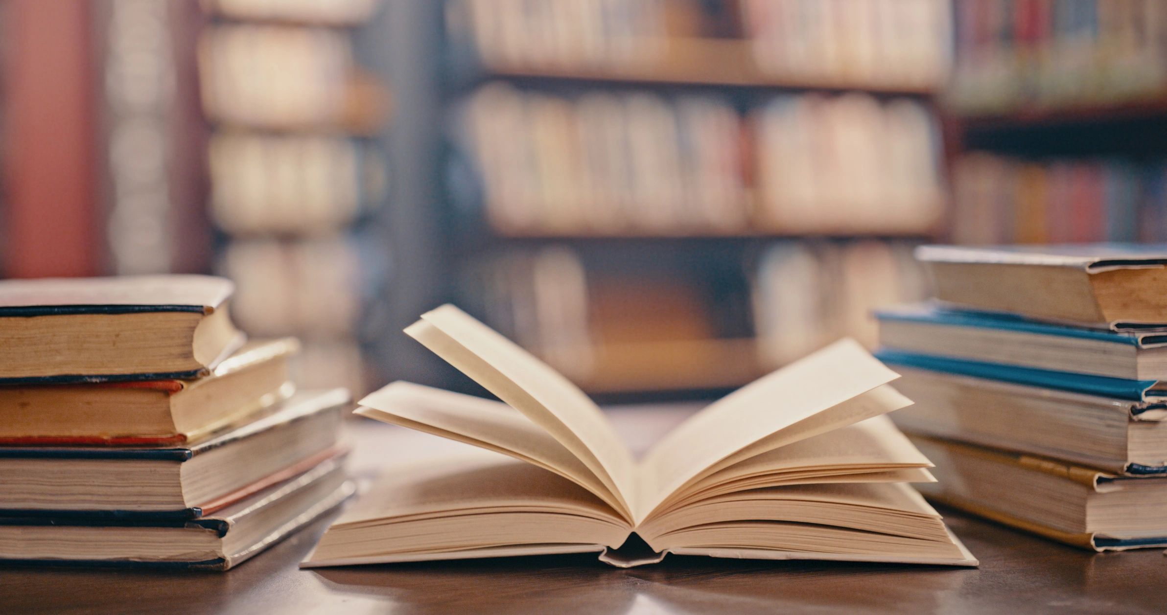 Open book and stacked books on a table in a library setting.