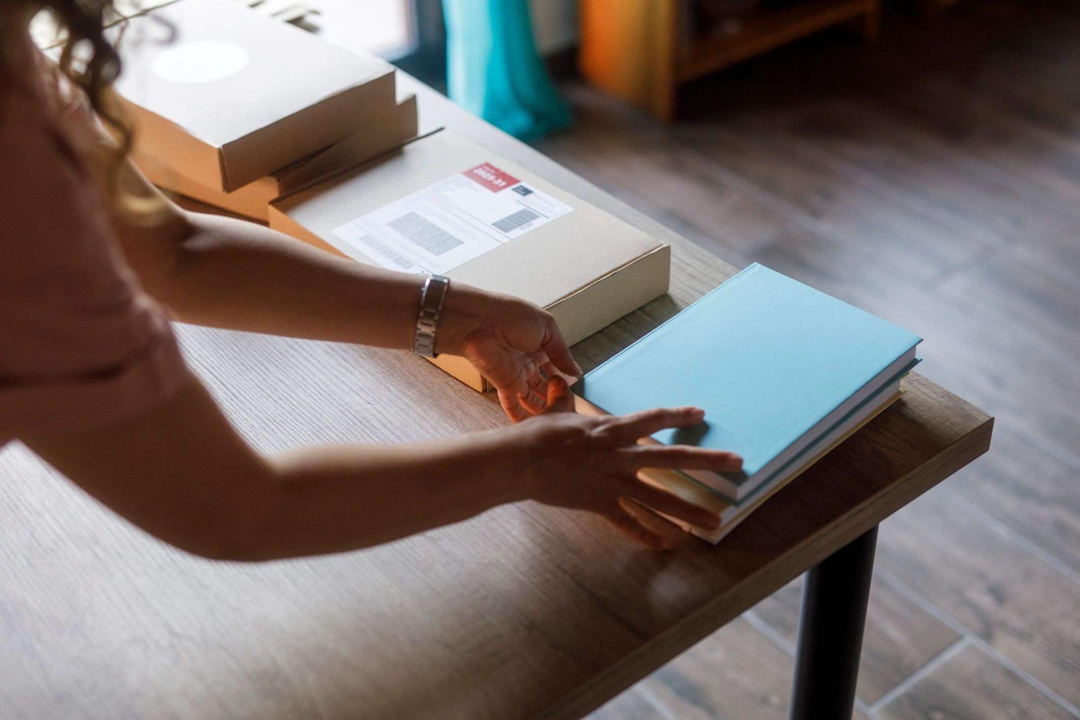 Hands packing notebooks for shipping at a small business desk.